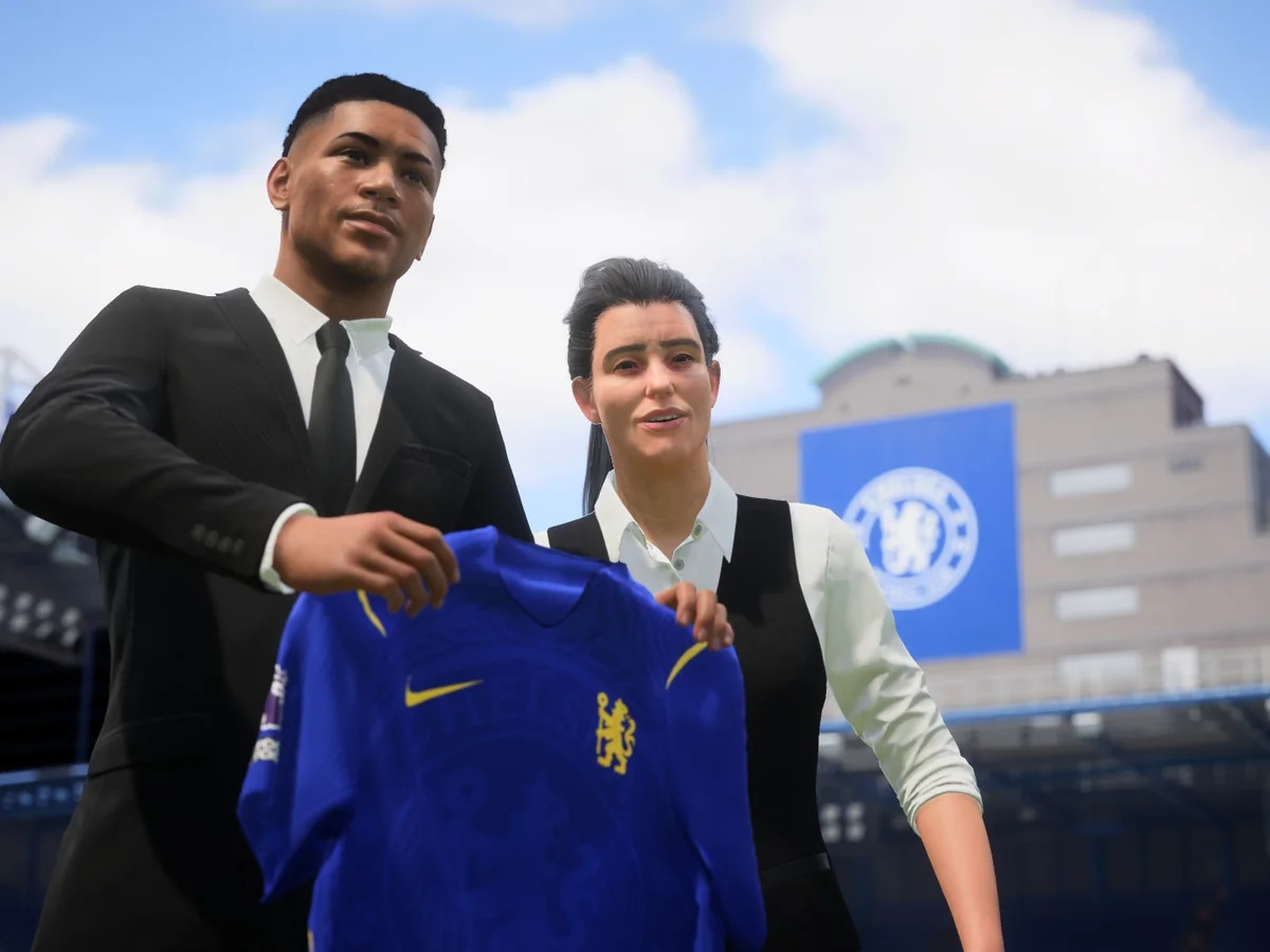 An EA SPORTS FC 27 player and club representative hold up a blue Chelsea shirt during a signing presentation.