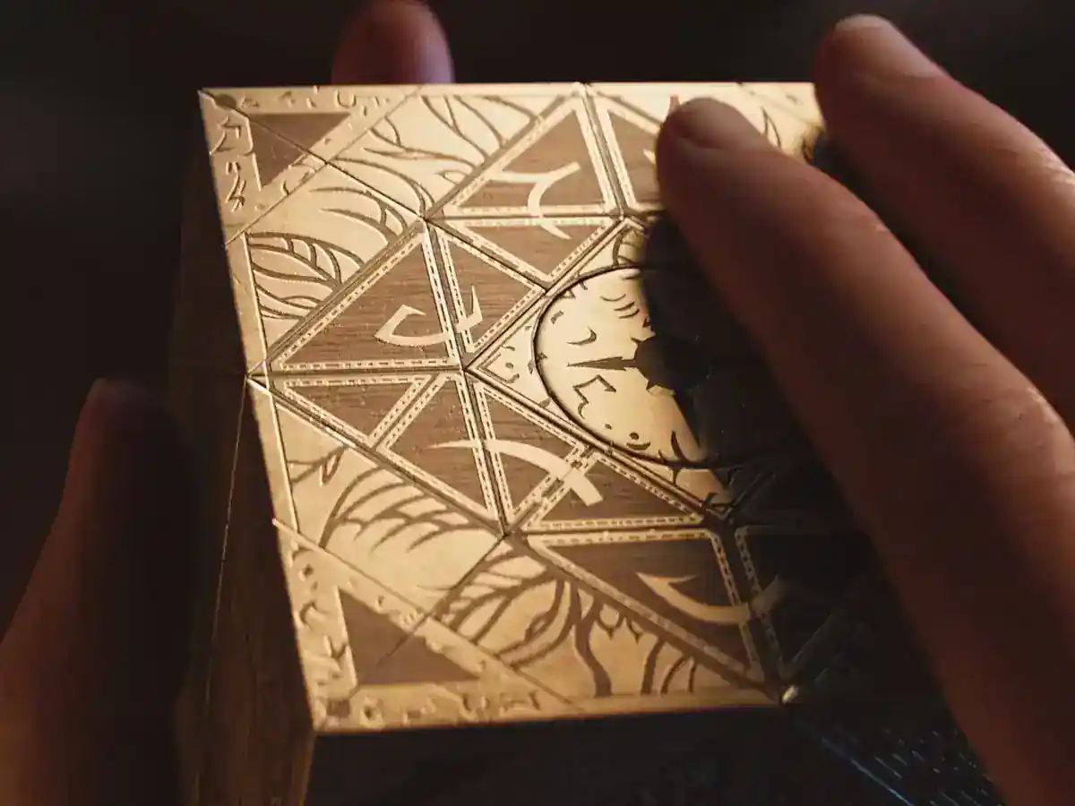 A hand reaches toward an ornate puzzle box in Hellraiser: Revival artwork.