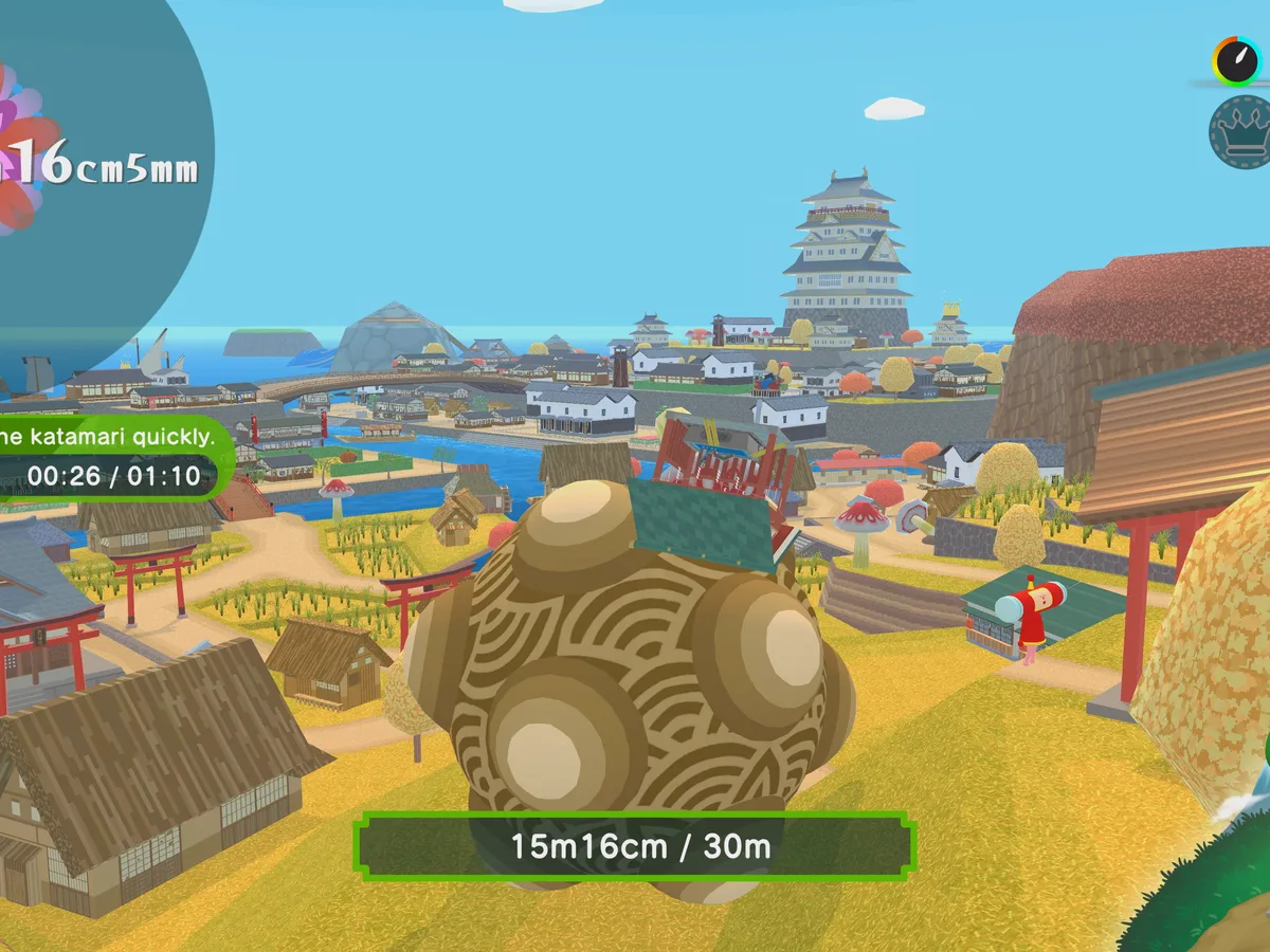 A large katamari rolls through a Japanese town with rooftops and fields in the background.