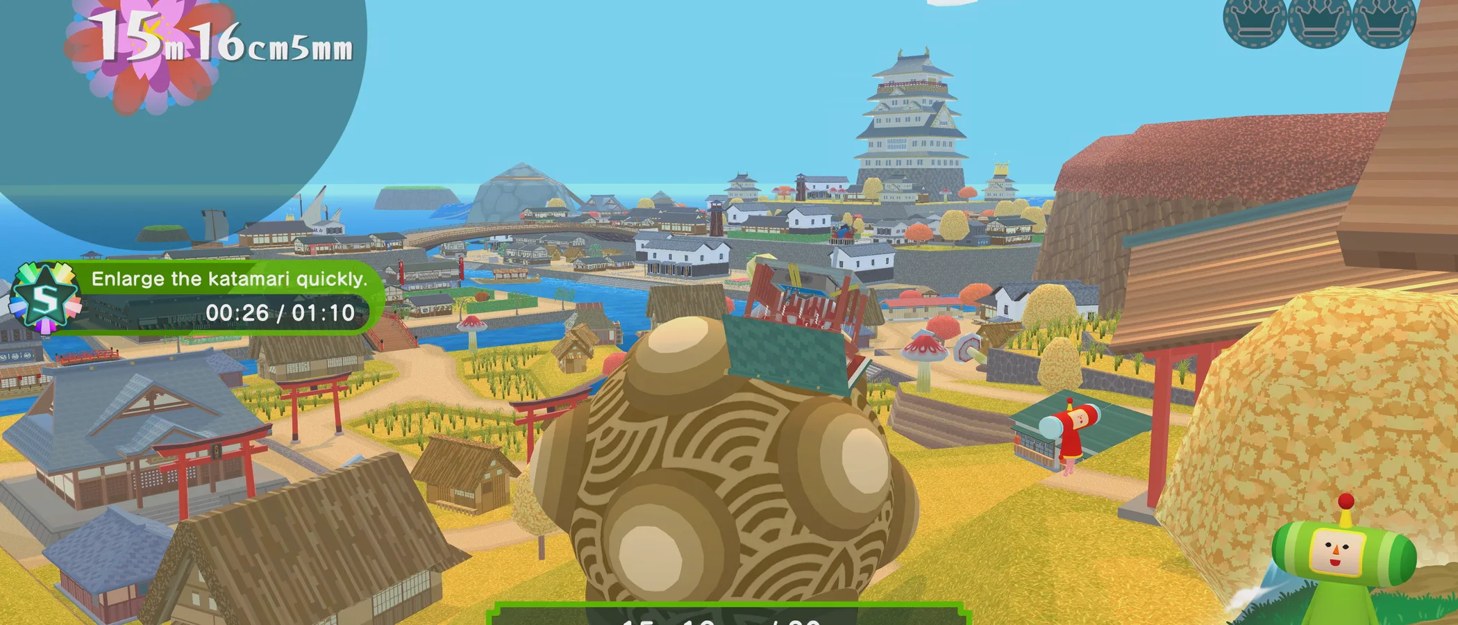 A large katamari rolls through a Japanese town with rooftops and fields in the background.