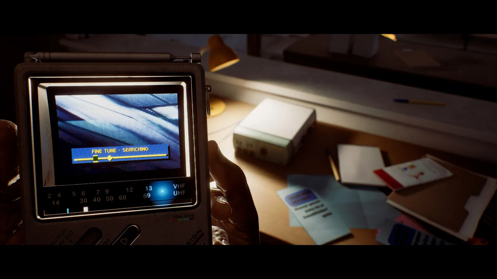 A CRTV pocket television displays a tuning signal beside scattered papers and cassette tapes in Silent Hill: Townfall.