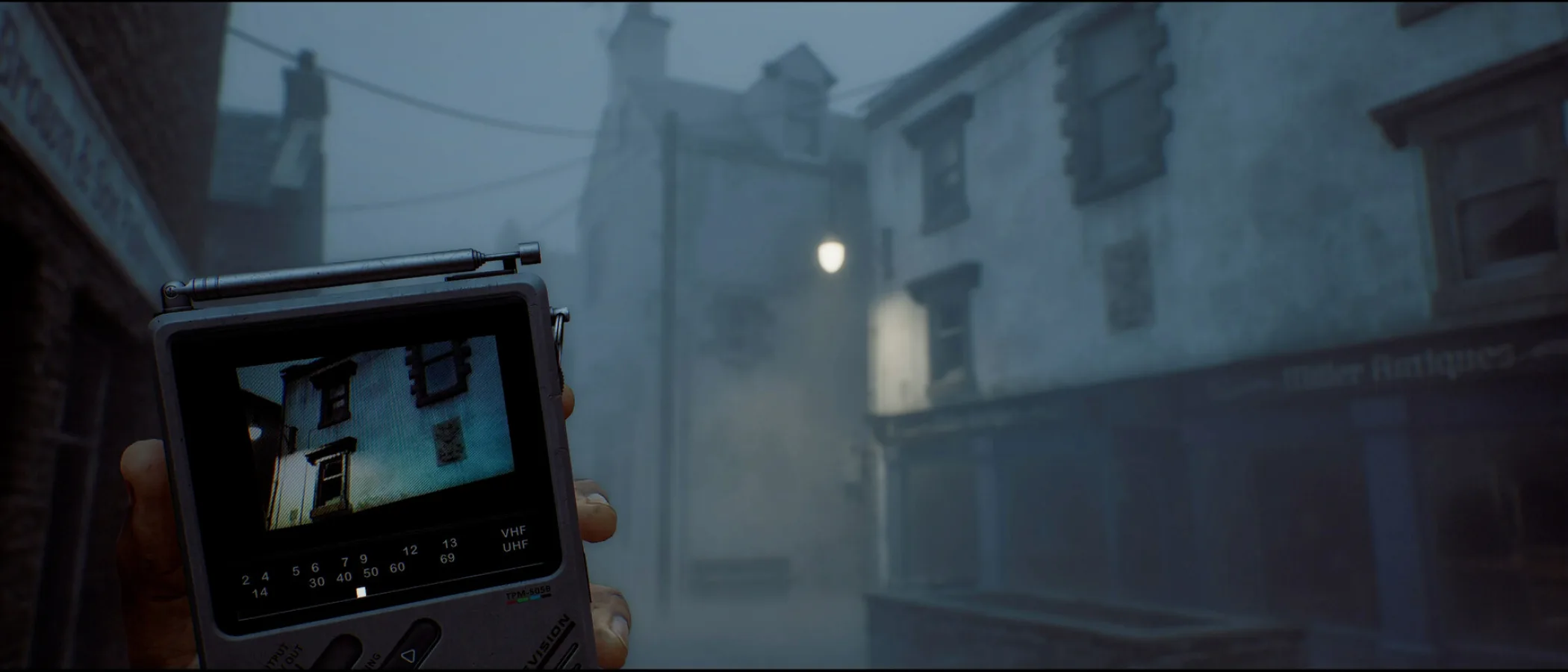 A CRTV pocket television is held up on a foggy street lined with old buildings in Silent Hill: Townfall.