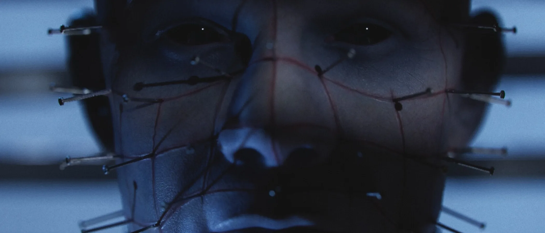A close-up official game image of Pinhead, his face framed by pins and dark blue light.