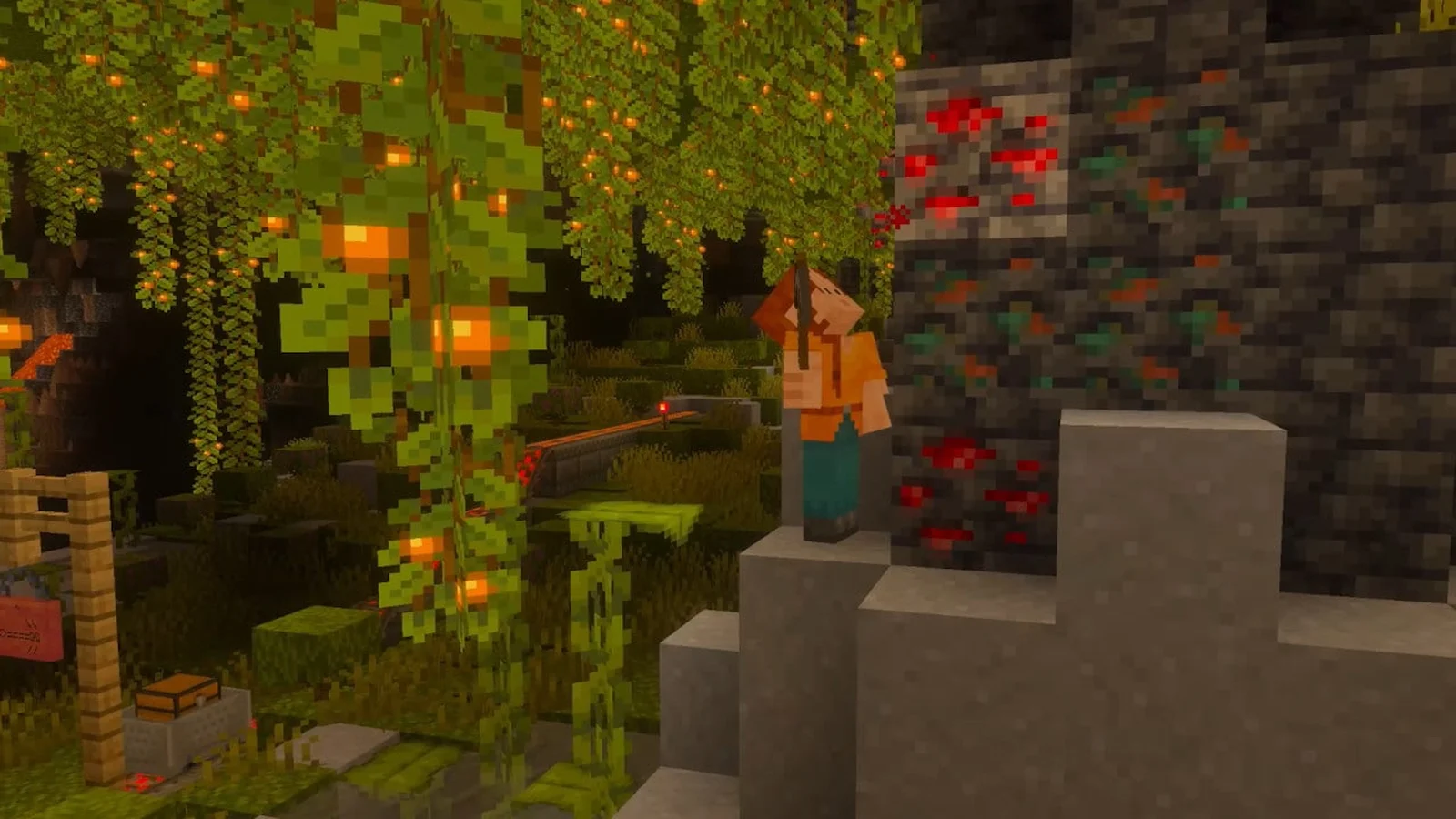 A Minecraft character stands beside glowing cave vines and colourful ore blocks in a dark cave.