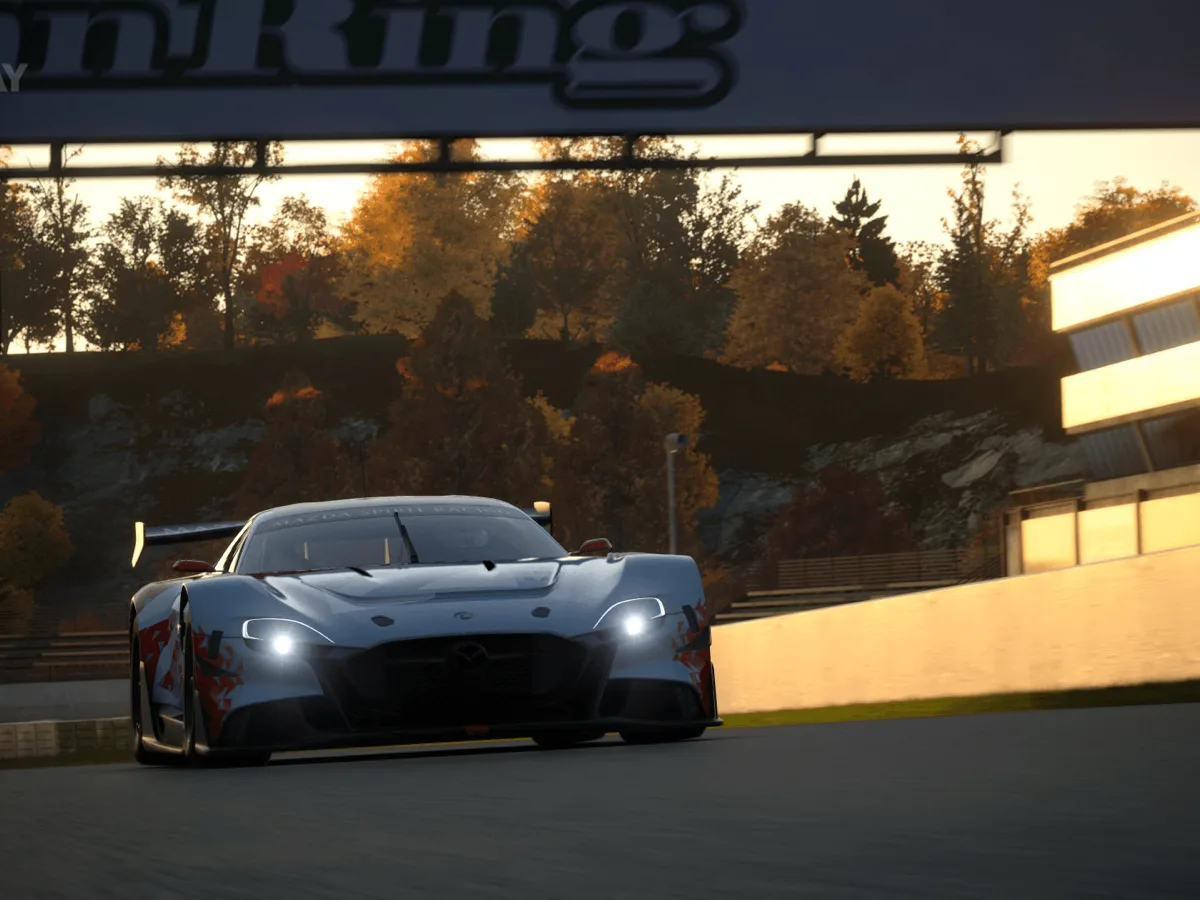 A racing car approaches a corner on an autumnal Gran Turismo 7 circuit at sunset.