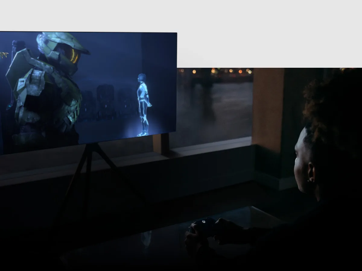 A person with a controller plays an Xbox game on a large television in a living room.